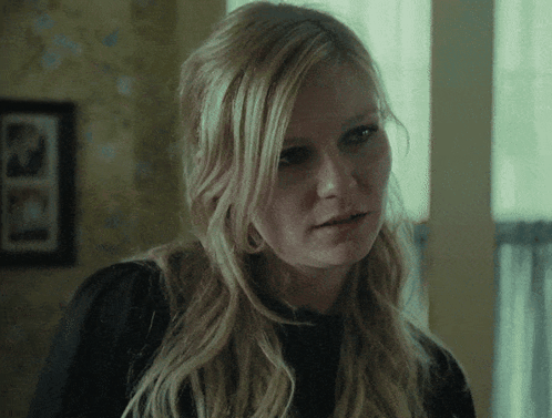 A Close Up Of A Woman 'S Face With A Picture Of A Man On The Wall Behind Her GIF