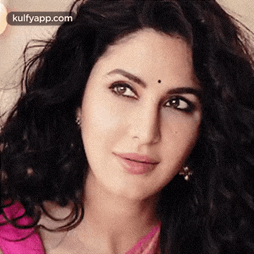 A Close Up Of A Woman 'S Face With A Pink Shirt And Earrings . GIF