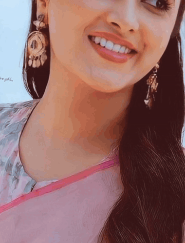 A Close Up Of A Woman 'S Face With A Pink Shirt And Earrings GIF