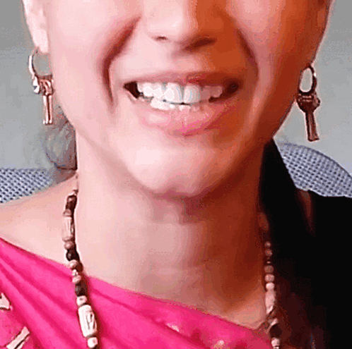 A Close Up Of A Woman 'S Face With A Pink Shirt And Earrings With Keys On Them GIF