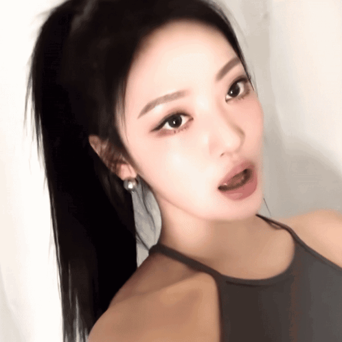 A Close Up Of A Woman 'S Face With A Ponytail And Earrings GIF
