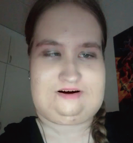 A Close Up Of A Woman 'S Face With A Poster On The Wall Behind Her GIF