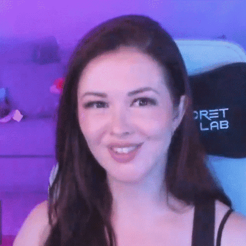 A Close Up Of A Woman 'S Face With A Purple Background And A Secret Lab Chair In The Background . GIF