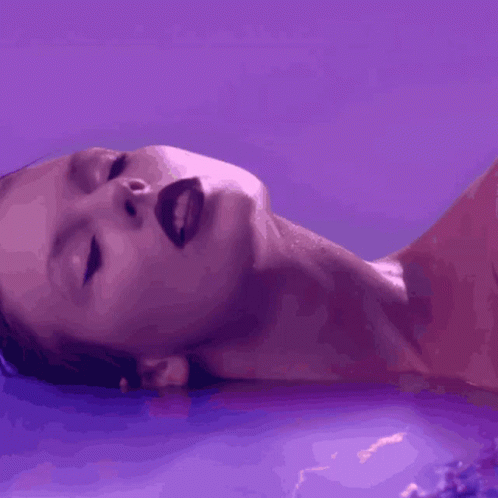 A Close Up Of A Woman 'S Face With A Purple Background GIF