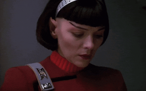 A Close Up Of A Woman 'S Face With A Red Sweater And A Strap That Says Xtc On It GIF