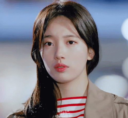 A Close Up Of A Woman 'S Face With A Striped Shirt And A Tan Jacket GIF