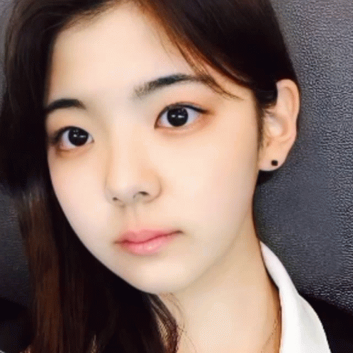 A Close Up Of A Woman 'S Face With A White Shirt And Black Earrings GIF