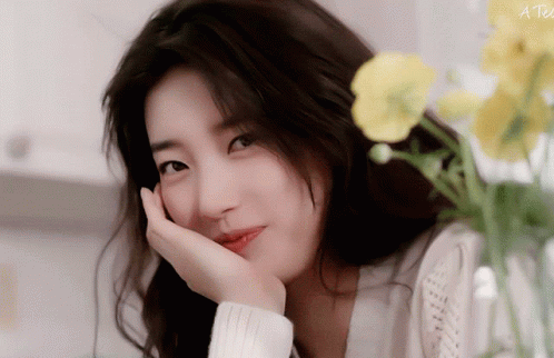 A Close Up Of A Woman 'S Face With A Yellow Flower In The Background And The Words A Tea On The Bottom Right GIF