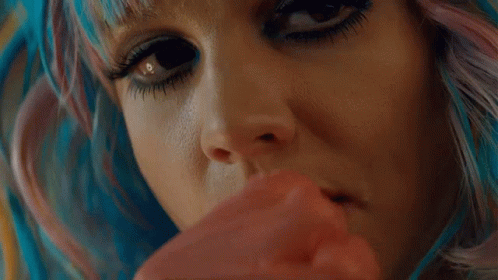 A Close Up Of A Woman 'S Face With Blue And Pink Hair Holding A Red Object . GIF