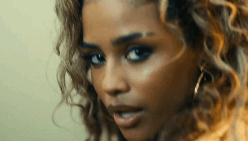 A Close Up Of A Woman 'S Face With Curly Hair And Earrings Looking At The Camera . GIF