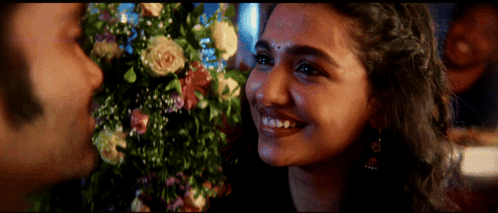 A Close Up Of A Woman 'S Face With Flowers In The Background GIF