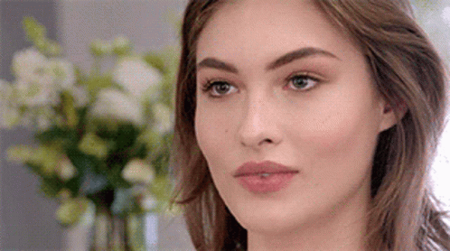 A Close Up Of A Woman 'S Face With Flowers In The Background . GIF
