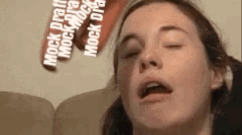 A Close Up Of A Woman 'S Face With Her Eyes Closed And A Sign Behind Her That Says `` Mock Draft '' . GIF
