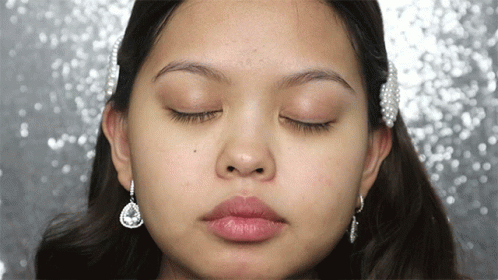 A Close Up Of A Woman 'S Face With Her Eyes Closed And Earrings GIF