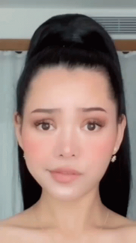 A Close Up Of A Woman 'S Face With Her Hair In A Bun And Earrings . GIF
