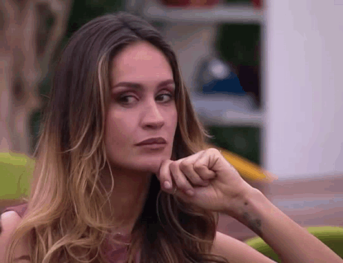 A Close Up Of A Woman 'S Face With Her Hand On Her Chin Looking At The Camera . GIF