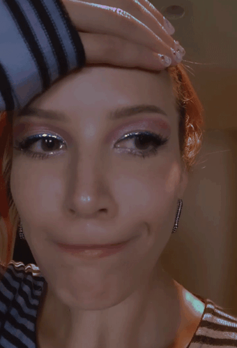 A Close Up Of A Woman 'S Face With Her Hand On Her Head GIF