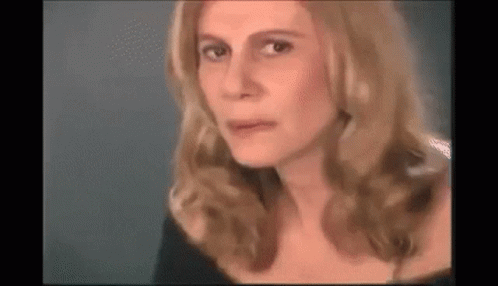 A Close Up Of A Woman 'S Face With Long Blonde Hair And A Black Dress . GIF