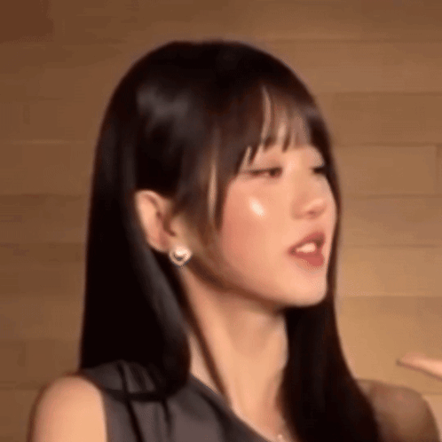 A Close Up Of A Woman 'S Face With Long Hair And Earrings Against A Wooden Wall . GIF