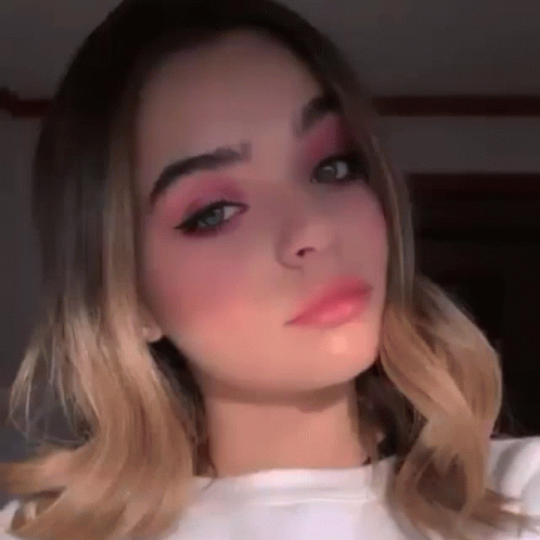 a close up of a woman 's face with pink eye shadow and a white shirt .