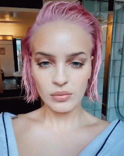 A Close Up Of A Woman 'S Face With Pink Hair And Blue Eyes GIF