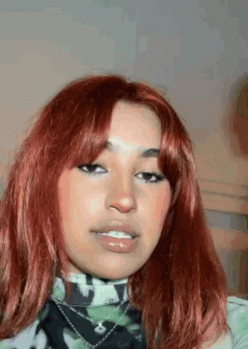 a close up of a woman 's face with red hair and a camouflage shirt .