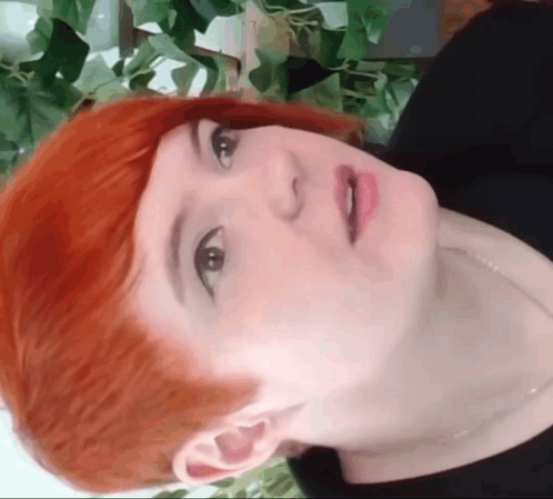 A Close Up Of A Woman 'S Face With Red Hair And Black Shirt GIF