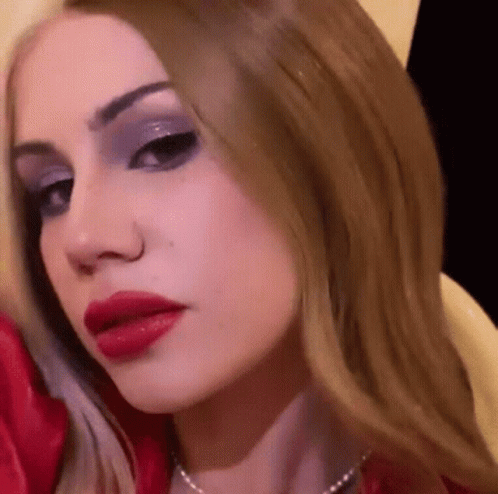 A Close Up Of A Woman 'S Face With Red Lipstick And A Pearl Necklace . GIF