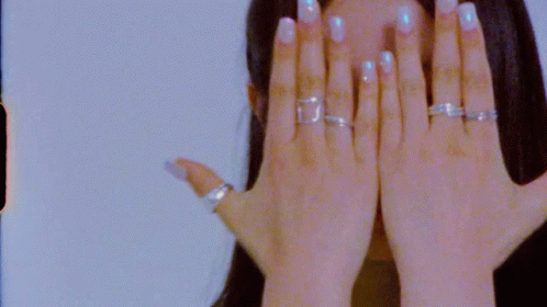 A Close Up Of A Woman 'S Hand With Rings On It Covering Her Face . GIF