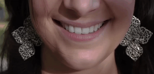 A Close Up Of A Woman 'S Mouth Wearing Earrings And Smiling GIF