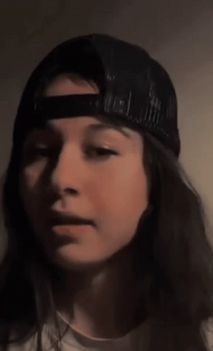 A Close Up Of A Woman Wearing A Baseball Cap Covering Her Mouth With Her Hand . GIF