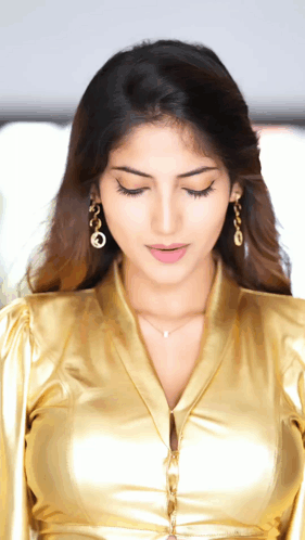 A Close Up Of A Woman Wearing A Gold Shirt And Earrings GIF
