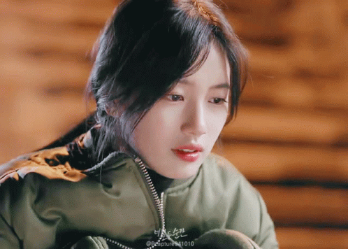 A Close Up Of A Woman Wearing A Green Jacket With The Number 1010 On The Bottom Right GIF