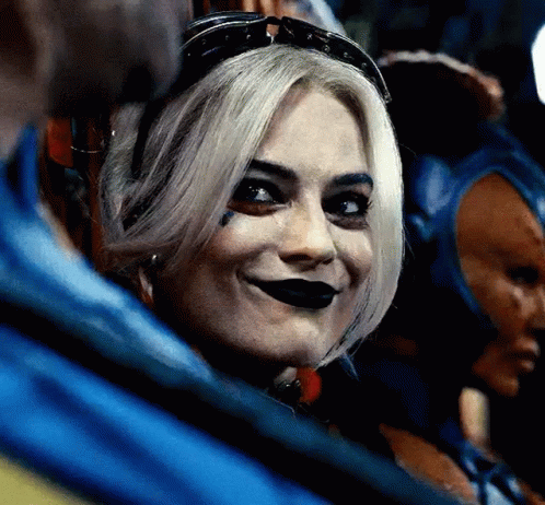 A Close Up Of A Woman Wearing A Harley Quinn Costume And Sunglasses Smiling . GIF