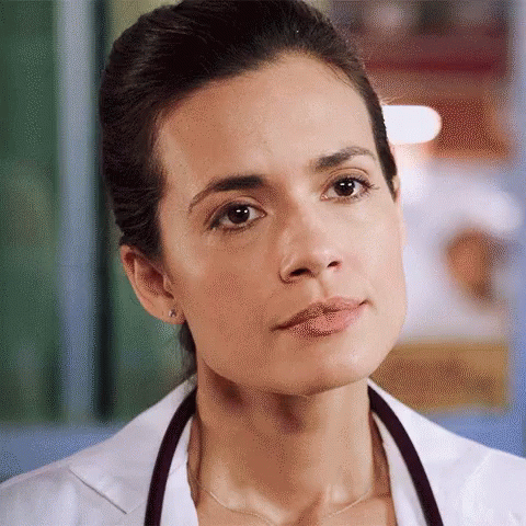 A Close Up Of A Woman Wearing A Lab Coat And Stethoscope Around Her Neck GIF
