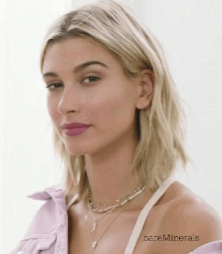 A Close Up Of A Woman Wearing A Purple Shirt And A Necklace With Bareminerals Written On Her Arm GIF