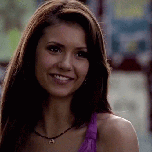 A Close Up Of A Woman Wearing A Purple Tank Top And A Necklace Smiling . GIF