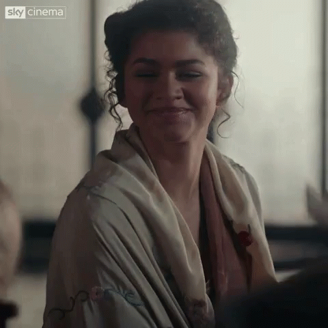 A Close Up Of A Woman Wearing A Scarf Around Her Neck And Smiling . GIF