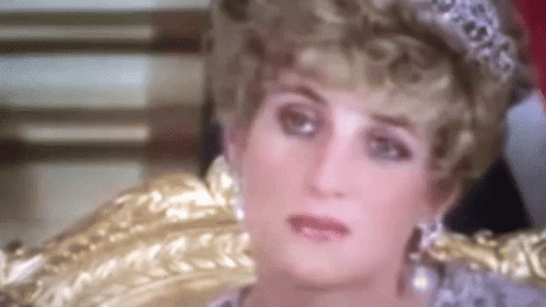 A Close Up Of A Woman Wearing A Tiara And Earrings Sitting In A Chair . GIF