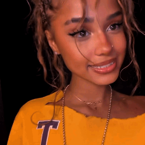 A Close Up Of A Woman Wearing A Yellow Shirt With The Letter T On It GIF