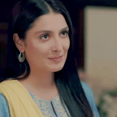 A Close Up Of A Woman Wearing Earrings And A Blue And Yellow Dress GIF