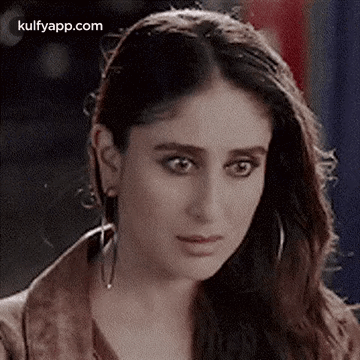 A Close Up Of A Woman Wearing Earrings And A Brown Jacket Looking At The Camera . GIF