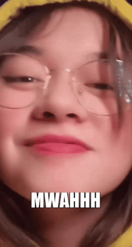 A Close Up Of A Woman Wearing Glasses And A Yellow Hoodie With The Words Mwahhh Written On Her Face . GIF