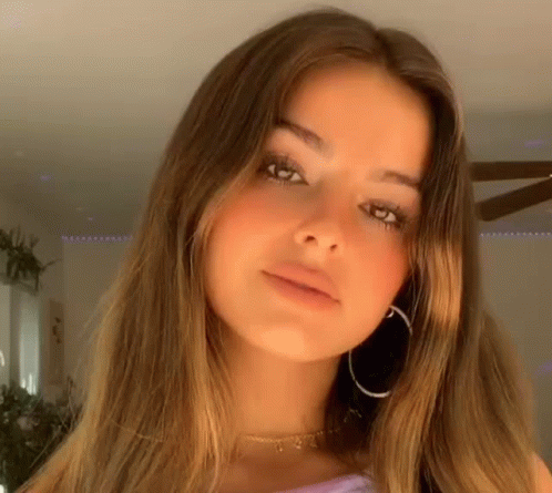 A Close Up Of A Woman Wearing Hoop Earrings And A Choker Looking At The Camera . GIF