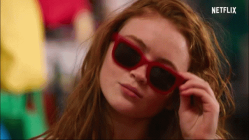 A Close Up Of A Woman Wearing Red Sunglasses With A Netflix Logo In The Corner GIF