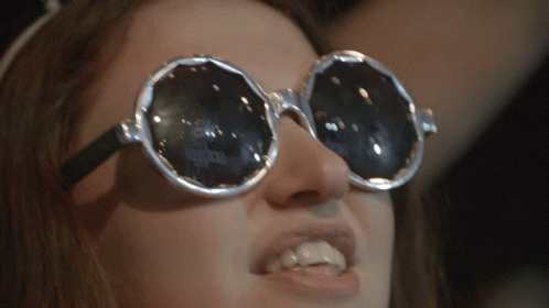A Close Up Of A Woman Wearing Sunglasses With A Reflection Of A Person 'S Face In Them GIF