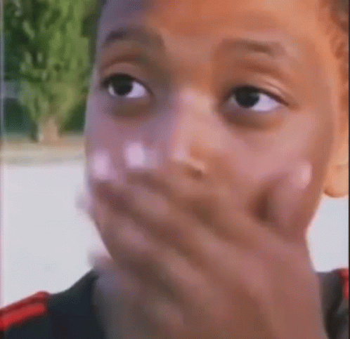 A Close Up Of A Young Boy Covering His Mouth With His Hand . GIF