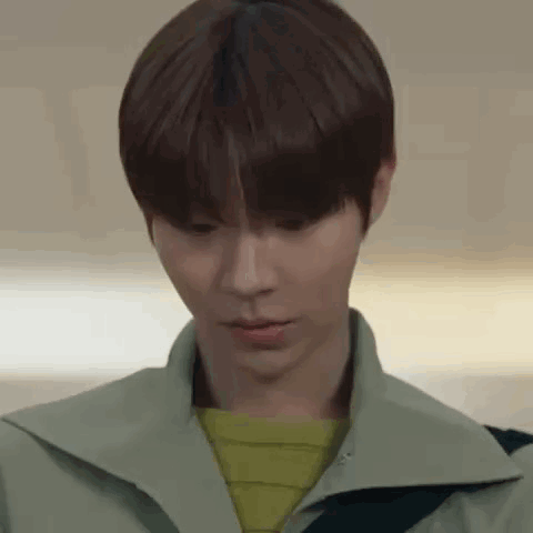 A Close Up Of A Young Man 'S Face Wearing A Green Jacket And A Yellow Sweater . GIF