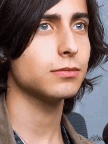 a close up of a young man 's face with blue eyes and long black hair .