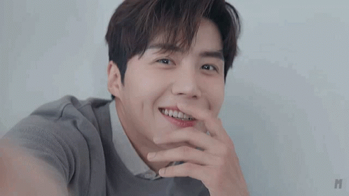 A Close Up Of A Young Man Smiling With His Hand On His Mouth . GIF